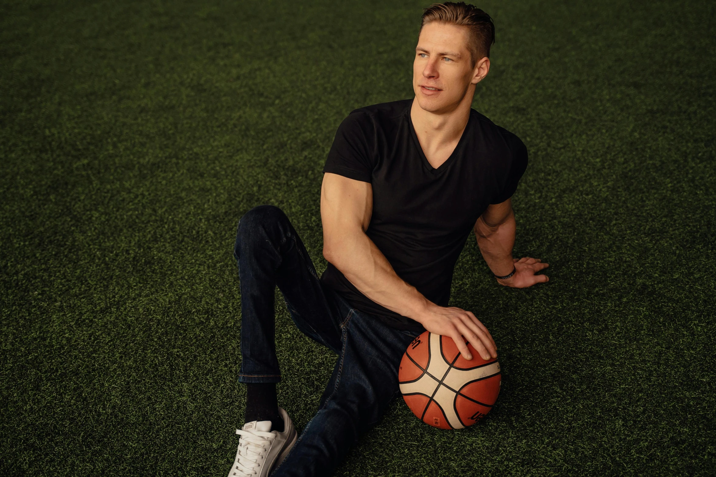 the man is sitting in the grass posing with his basketball