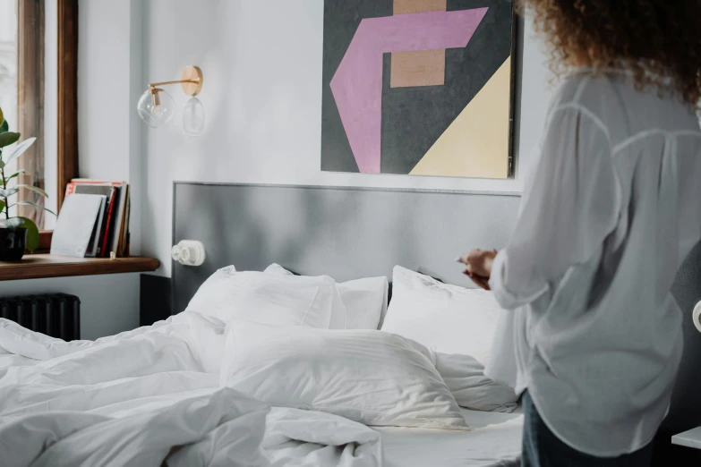 a woman stands in her bedroom as she looks at a painting