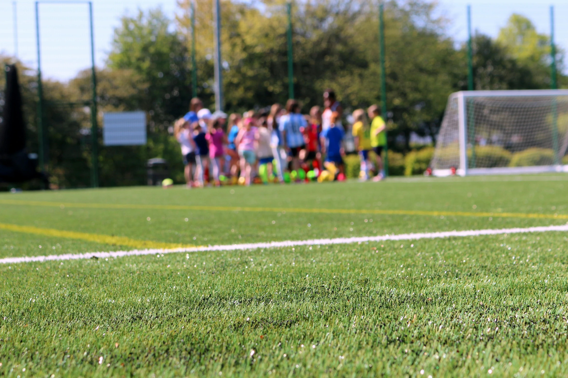 two children with a frisbee in their hands are on a soccer field as a group of people look on