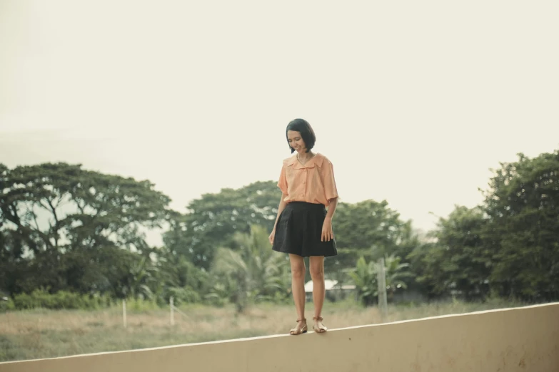 a young woman stands on a wall with her hand in her pocket and looks at the camera