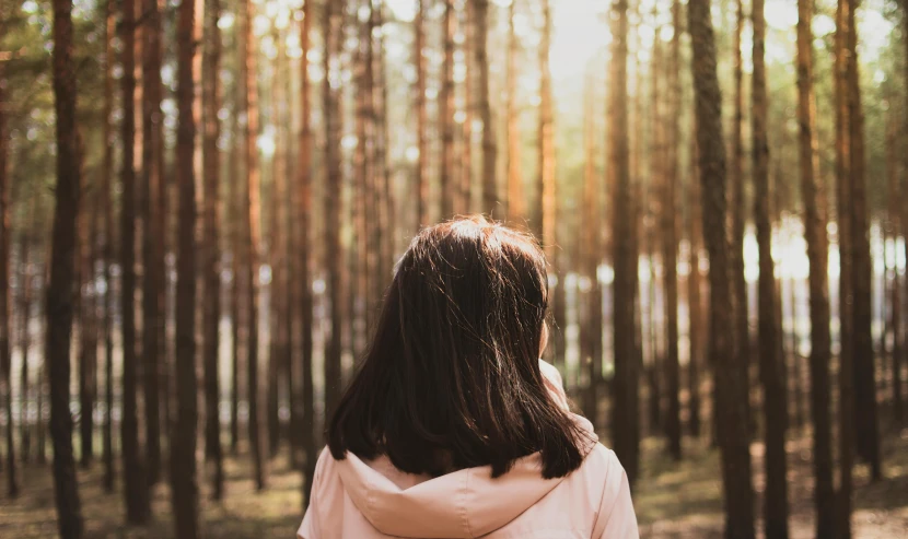 a woman wearing a coat in front of a forest