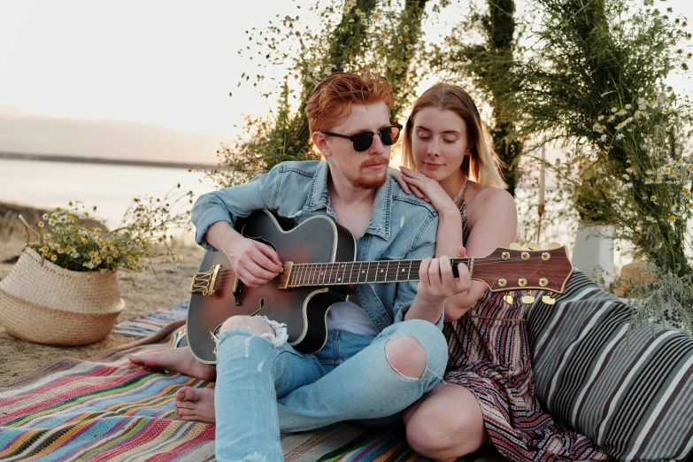 two people sit on the beach with a guitar