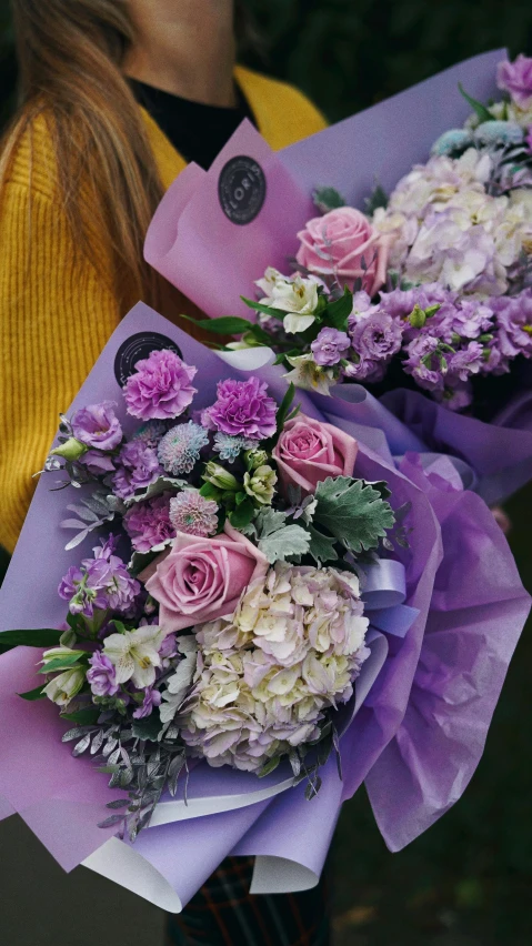 two woman hold flowers wrapped in purple wrapping