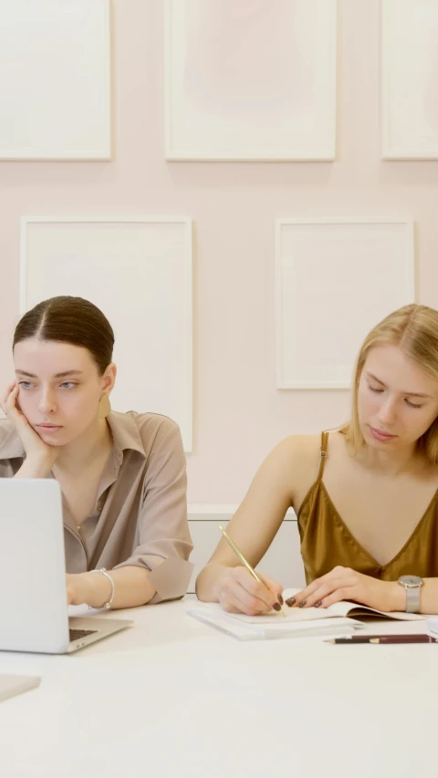 two women working on computer screens while sitting at a table