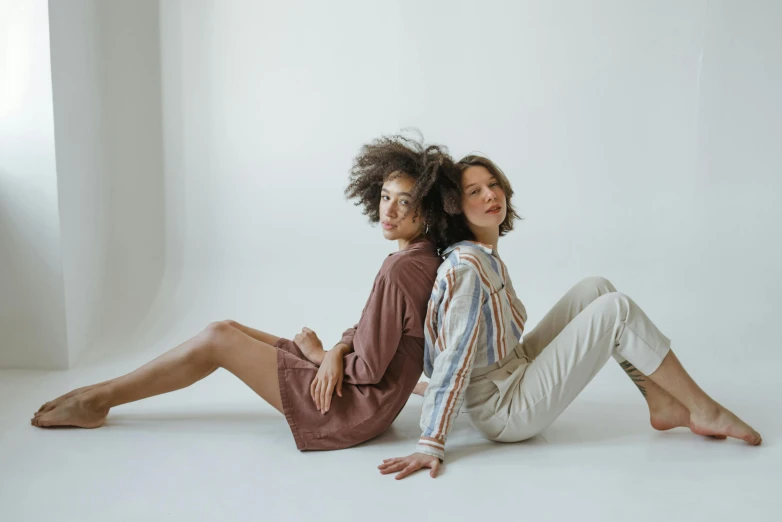 two women sitting on the floor in front of a white backdrop