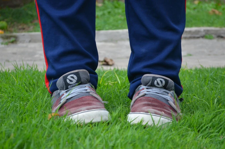 legs and shoes of a person in blue jeans with red converses standing in grass