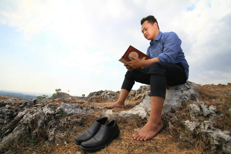 a man is sitting on top of a hill reading a book