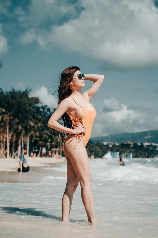 a young woman in a bodysuit and sunglasses poses on the beach