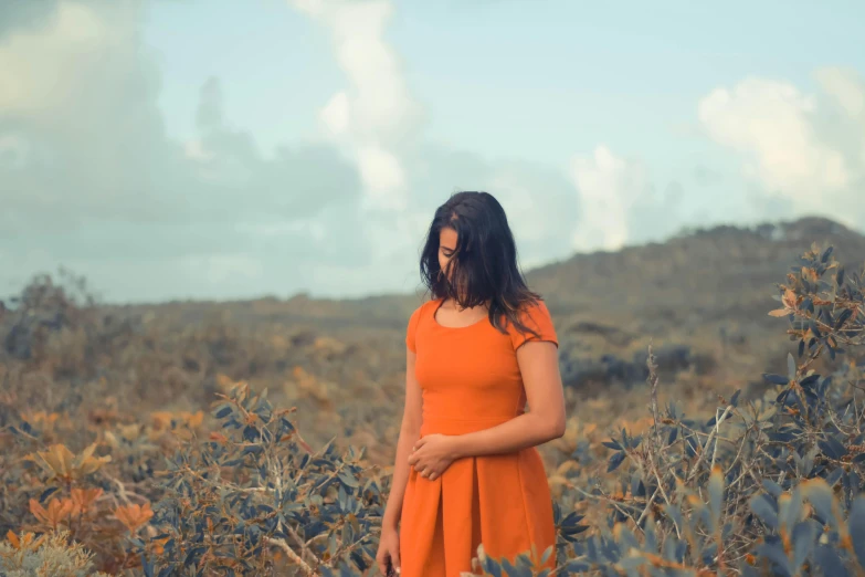 a young woman in an orange dress stands among tall plants