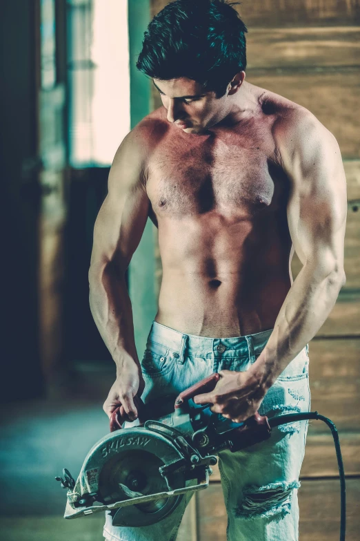 shirtless man holding metal piece while standing in a garage