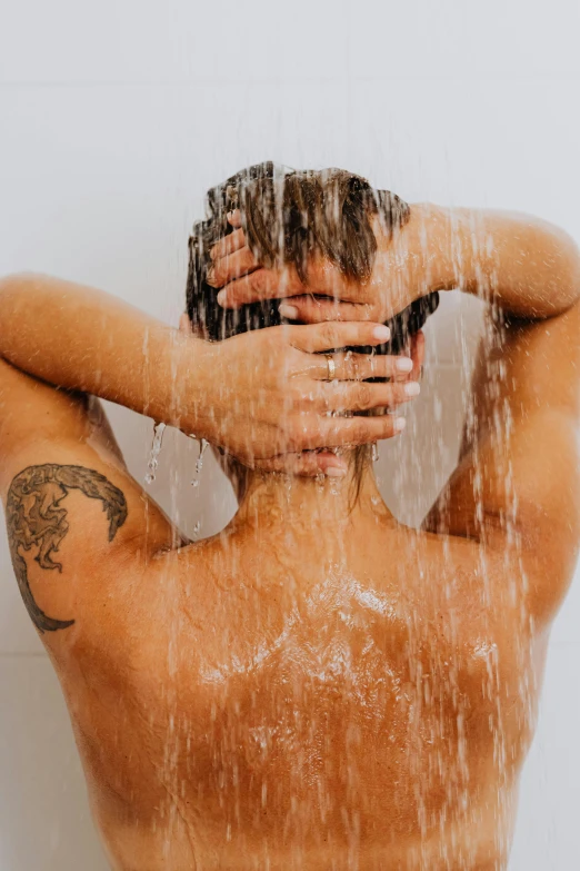 a shirtless man stands in front of a shower, with his hands on his face