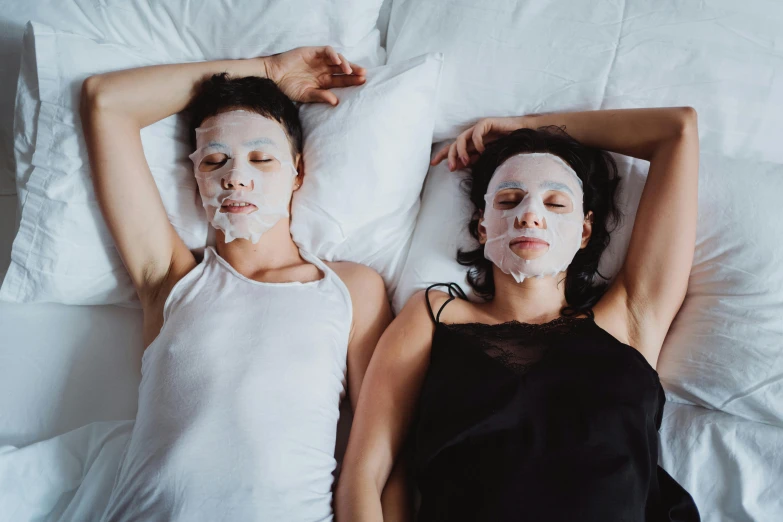 two people laying on top of a bed with facial masks on