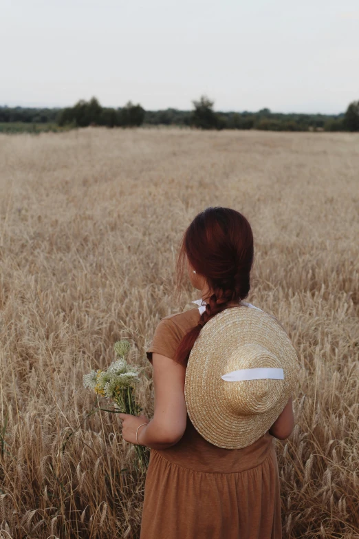 a woman with a large hat standing in a wheat field