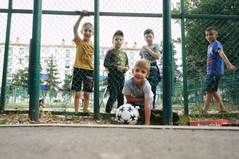 a group of children posing in front of a gate with a soccer ball