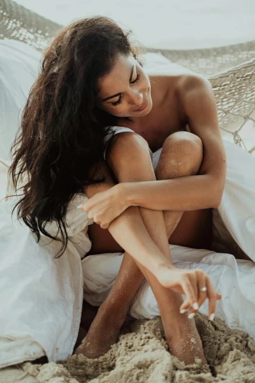 a beautiful woman sitting in a hammock on top of sand