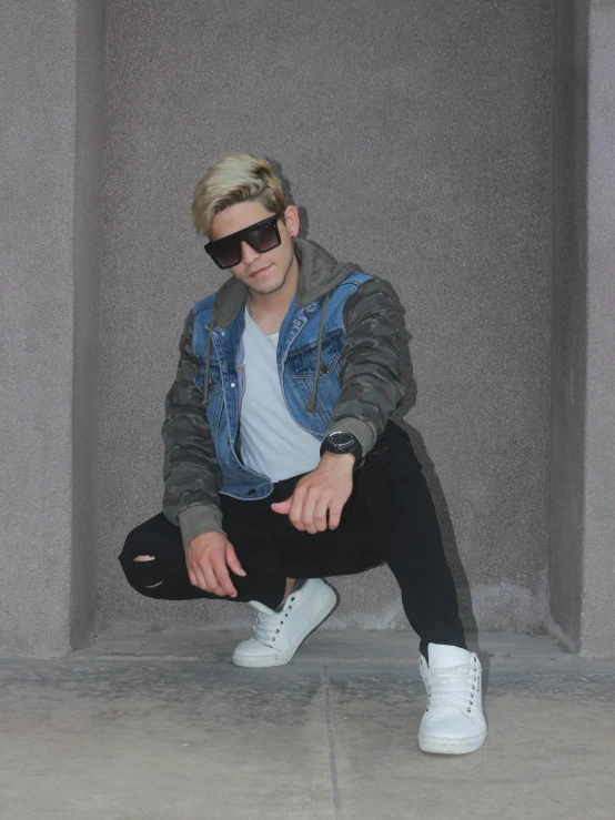 a man with blonde hair and sunglasses squatted on concrete