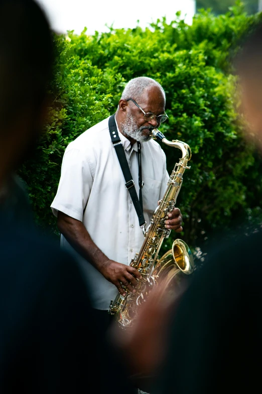 a man playing saxophone while standing in front of bushes