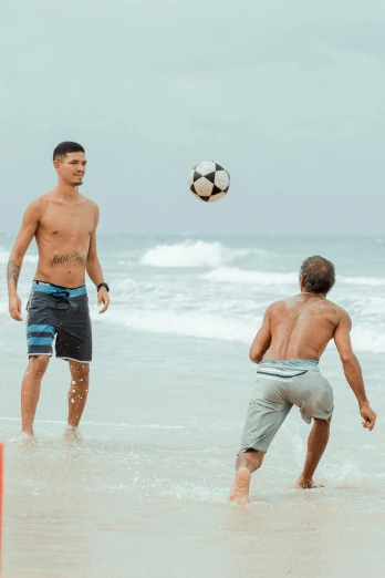 two shirtless men on the beach playing soccer