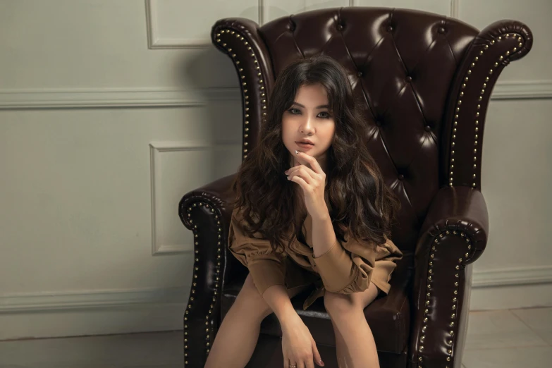 a pretty girl sitting in a chair with her hand under her chin