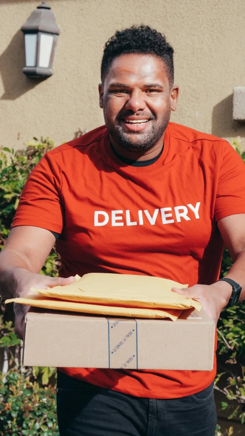 a man with an orange delivery shirt has a box of pizza