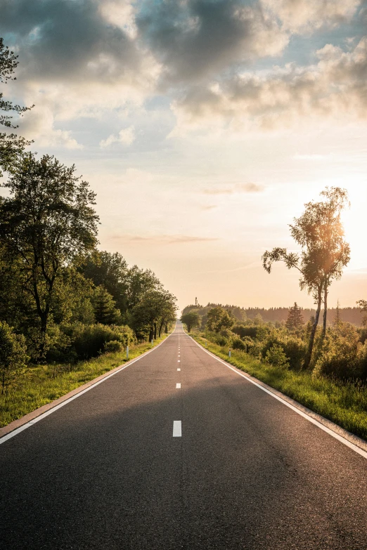 an empty road surrounded by green trees in the countryside