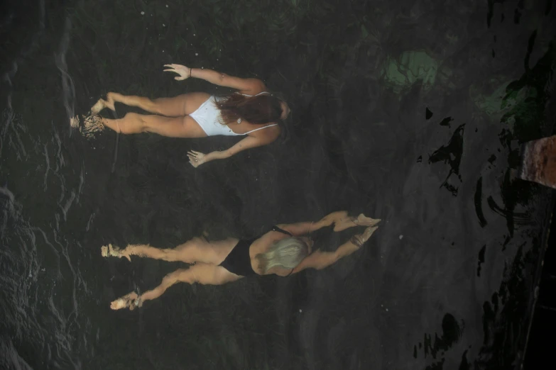 three young women in swim suits are laying by the water