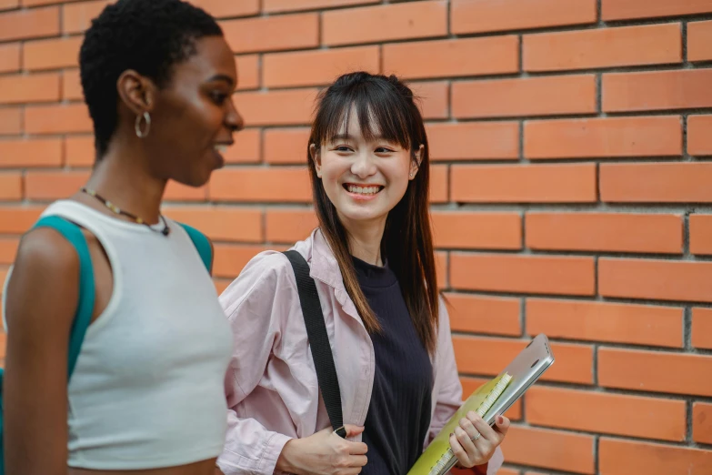 two women standing next to each other by a brick wall