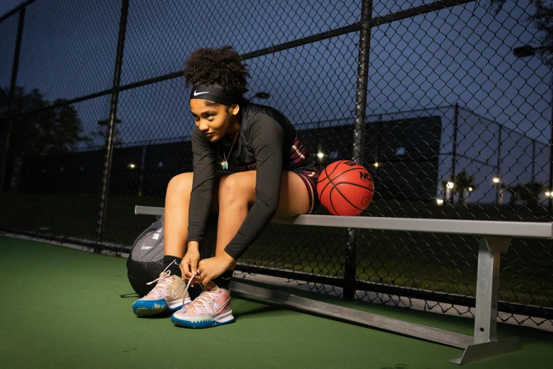 the basketball player is sitting down on the bench with her shoes and a ball