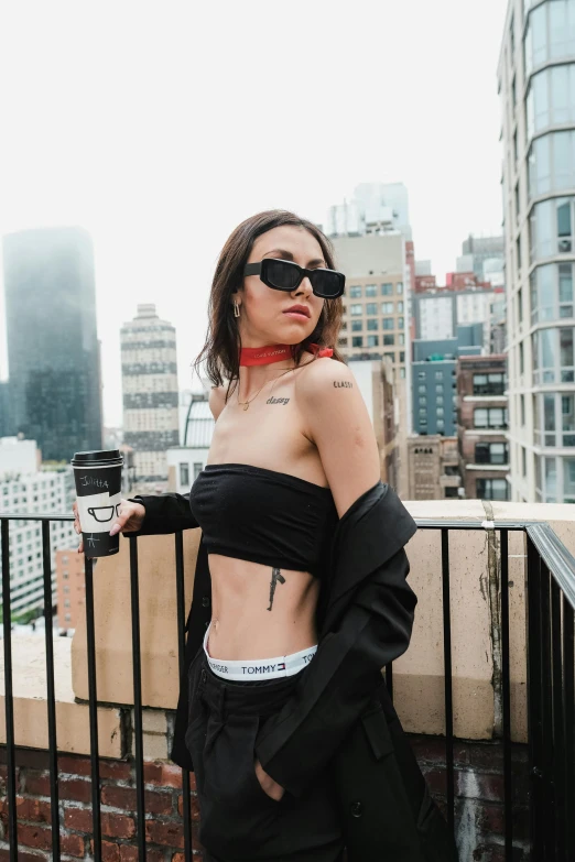 a woman wearing sunglasses and black clothing with a coffee cup