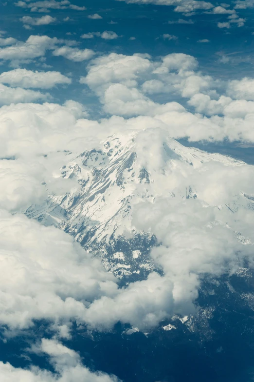 the top of a snowy mountain nestled over some clouds