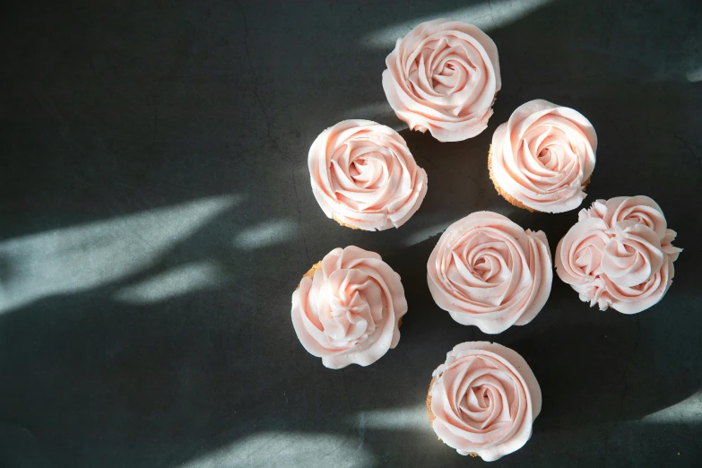 six cupcakes, with frosting sitting on a black surface