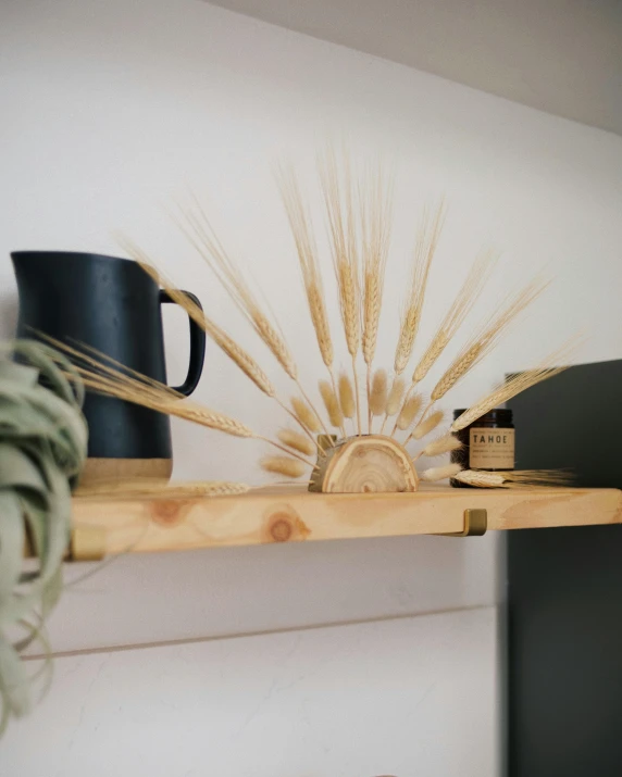 two black mugs sit on top of a shelf next to wheat stalks