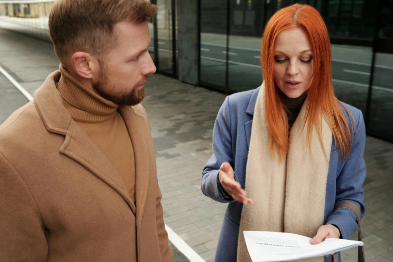 two people stand looking at papers on a sidewalk