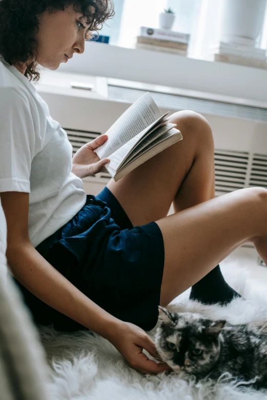 woman reads book while sitting on white fur rug with cat