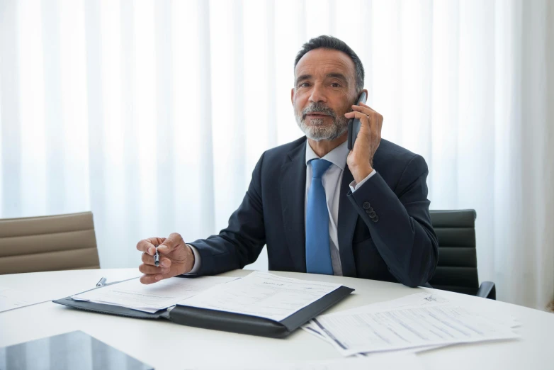 a man is sitting at a white table in an office talking on the phone