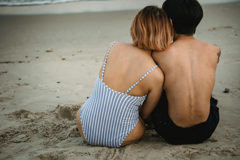 two people sitting on the beach in their bathing suits