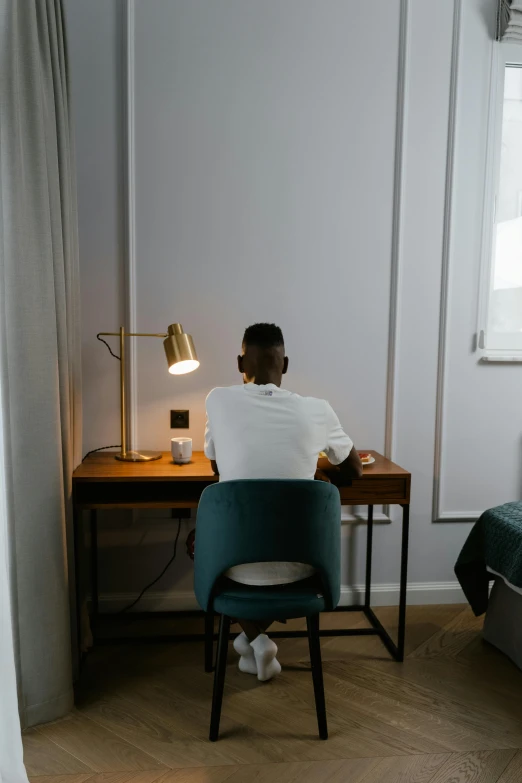 a man sitting at a small table in front of a wall with a lamp