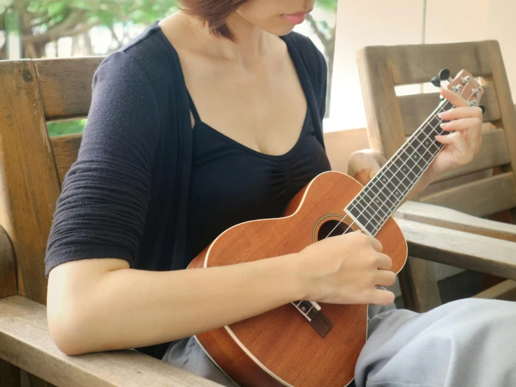 a woman sitting on a wooden bench playing a guitar