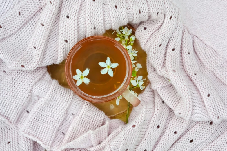 an orange colored beverage in a glass with flowers in it on a pink and white blanket