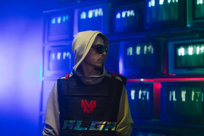 a man in sunglasses, sweater and vest stands in front of stacks of lights