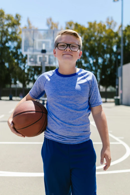 a boy in glasses holding a basketball on the court