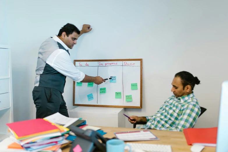 two men are sitting around a table writing on the white board