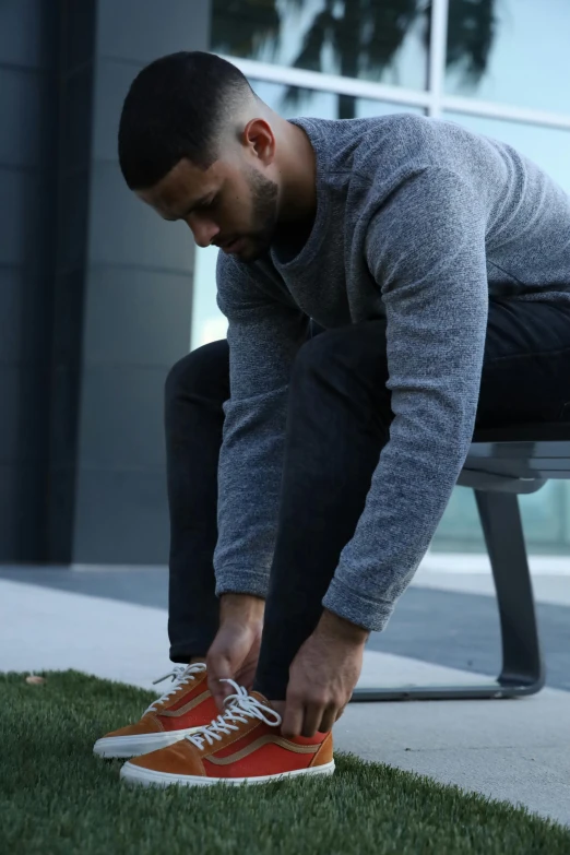 a man tying his shoes with an orange sneaker