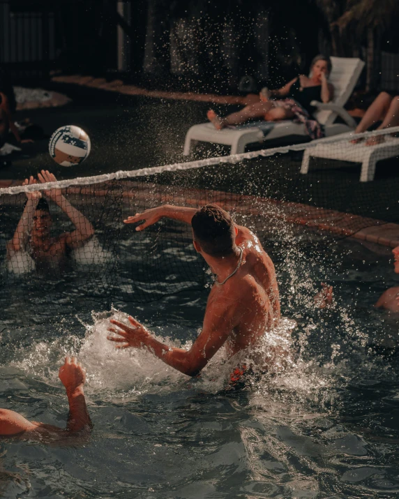 two men playing volleyball in the pool and people swimming