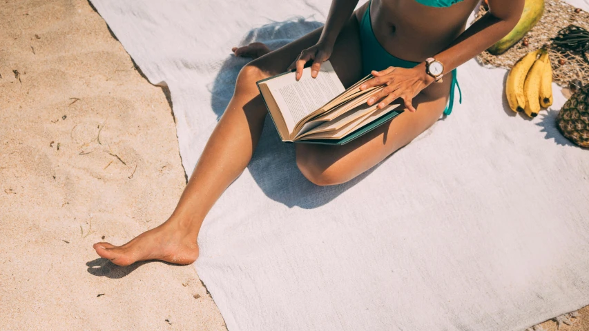 a woman sitting on top of a beach holding a book