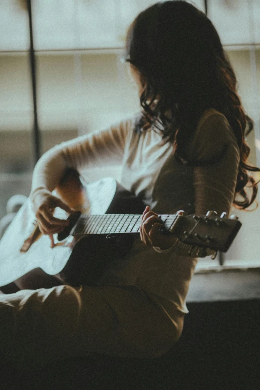 a woman is playing a guitar by a window