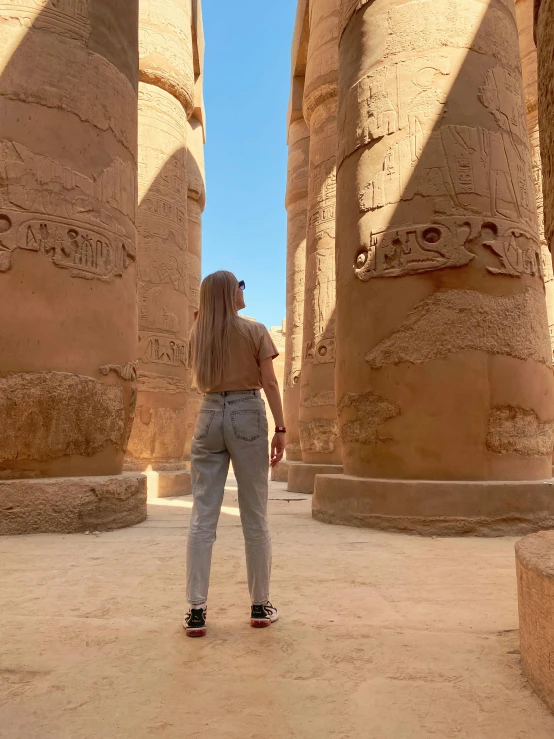 woman stands in the sun near some massive statues