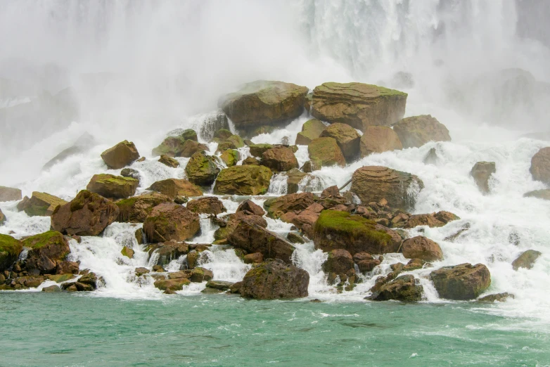 a person sitting on top of some rocks near a waterfall