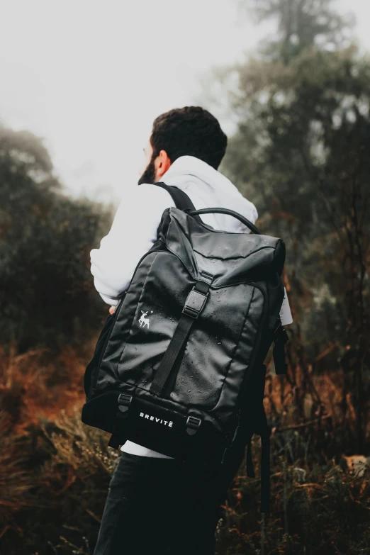 a man wearing a backpack, standing outdoors in a forest