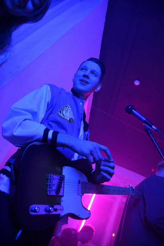 a young man with a guitar standing next to a microphone